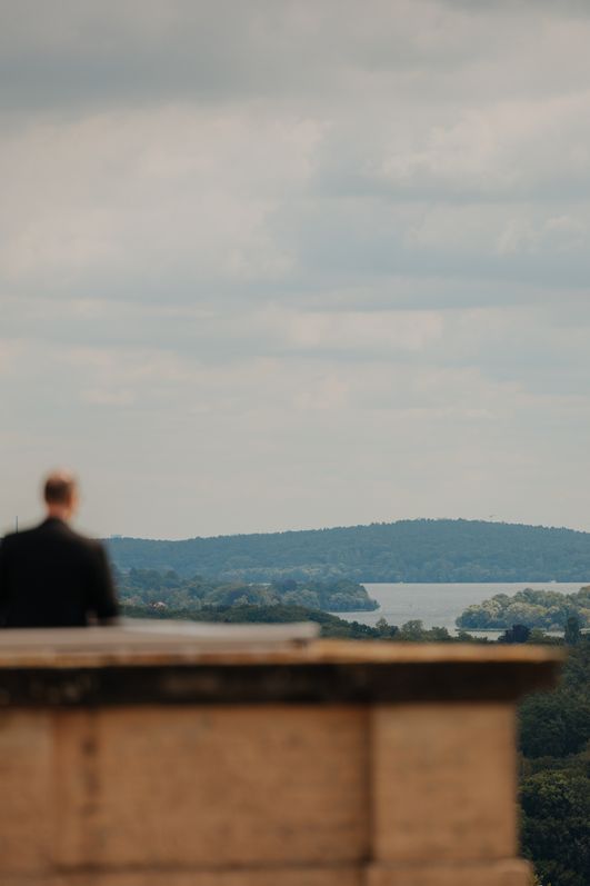 Zwei Personen blicken vom Belvedere Pfingstberg über Wälder, Seen und Berliner Skyline