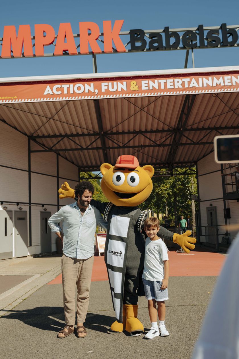 A family in front of the entrance to the Babelsberg film park with mascot