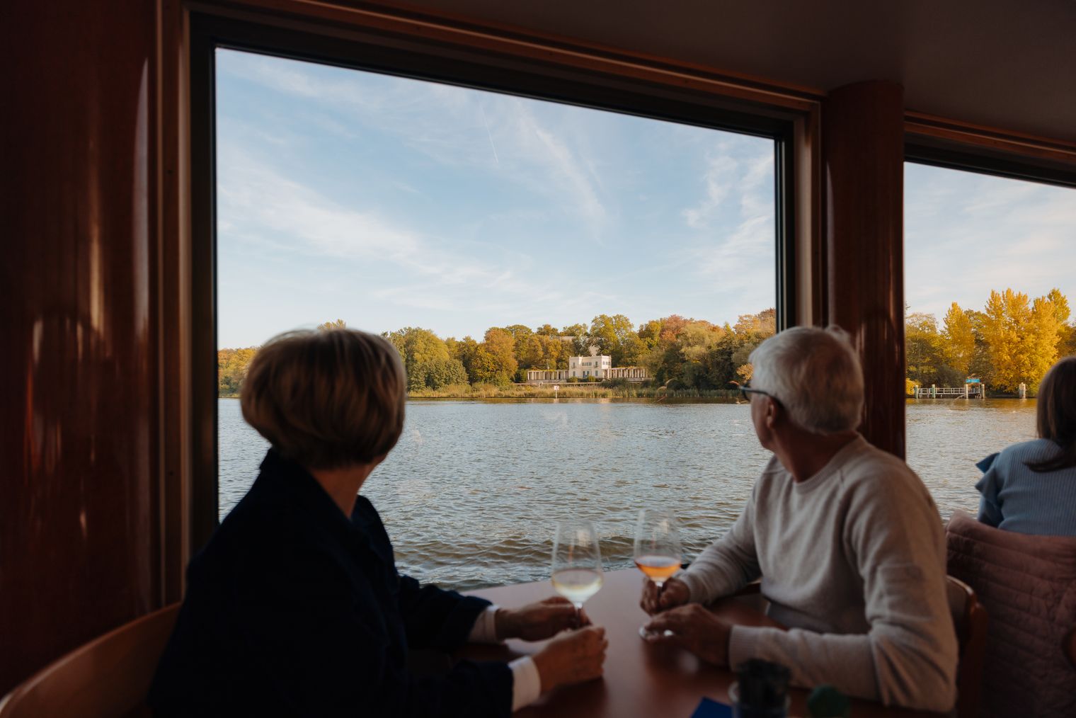 Eine Frau und ein Mann genießen ein Glas Wein auf einer herbstlichen Schifffahrt in Potsdam