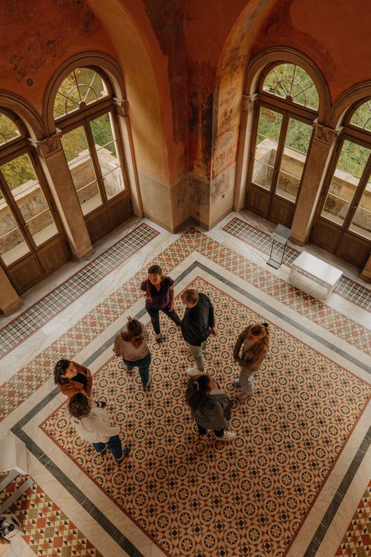 Gruppe im historischen Saal des Belvedere Pfingstberg mit Rundbogenfenstern und Mosaikboden