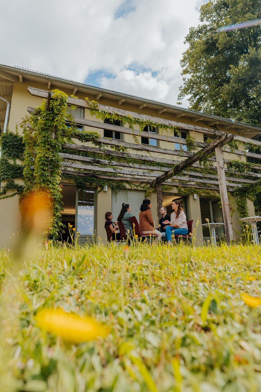 Menschen sitzen auf der Terrasse des Pfingstberghauses unter bewachsener Pergola
